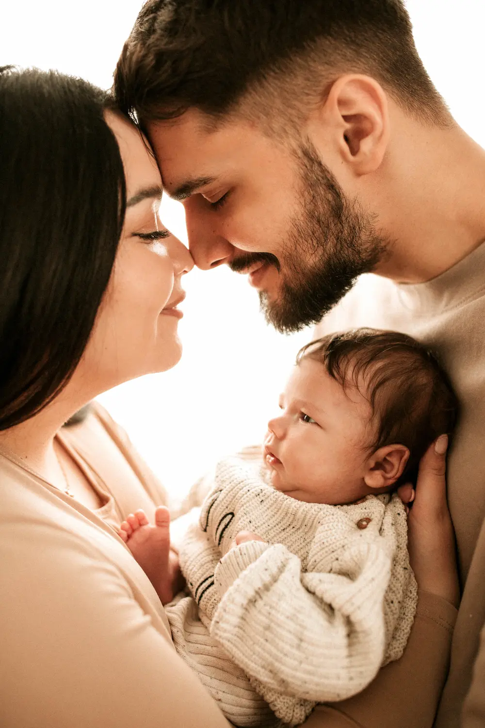 Para z miłością spogląda na swojego noworodka owiniętego w przytulny sweterek, tworząc ciepłą, intymną rodzinną chwilę.