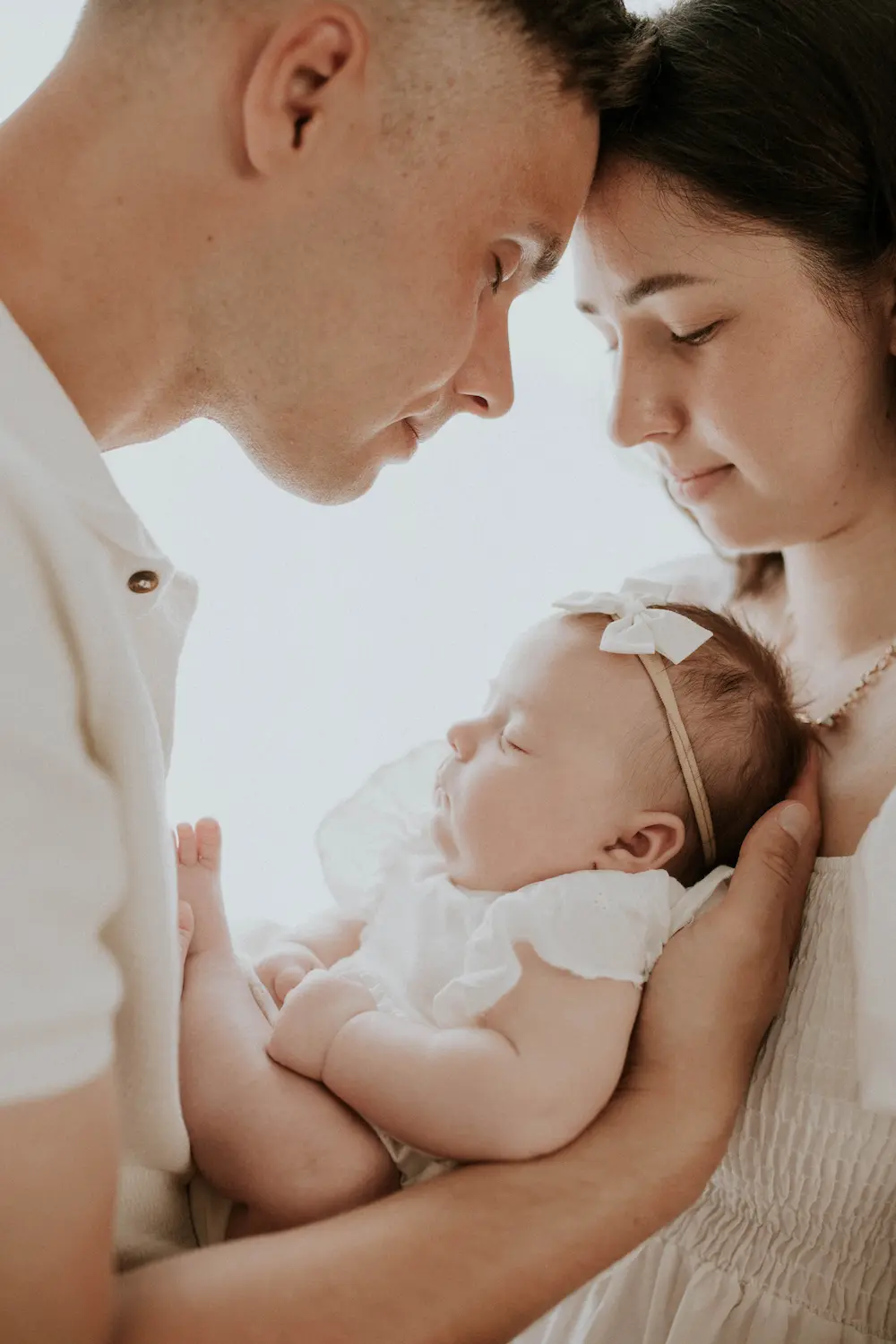 Czuła chwila przedstawiająca rodzica trzymającego śpiące niemowlę owinięte w miękki strój, przy delikatnym świetle w tle.